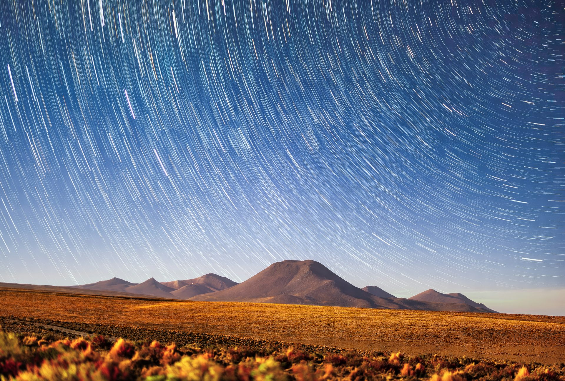 Star trails shine above mountains and the desert.