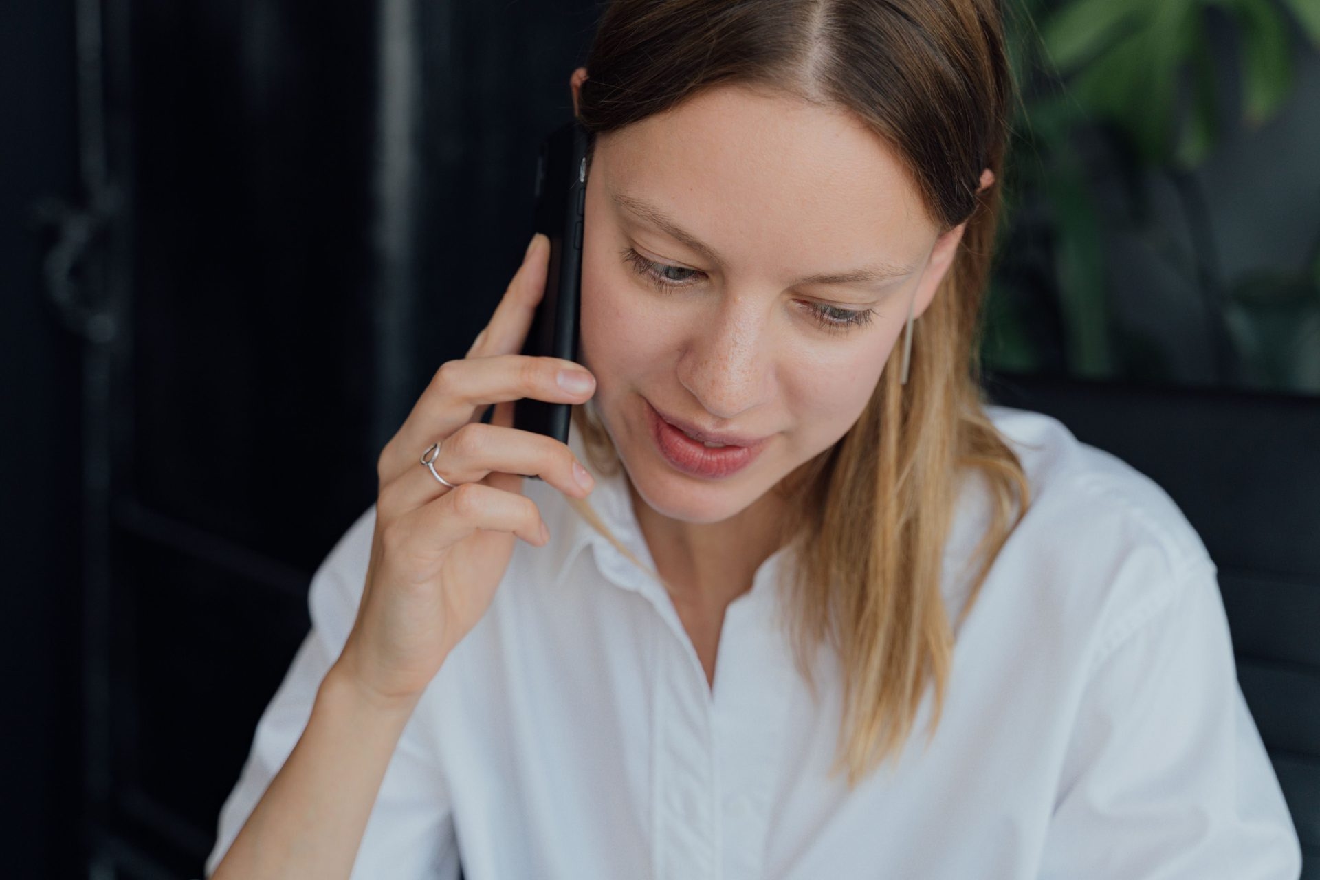 A professional woman in a white shirt making a phone call in an indoor setting, showing communication and business engagement.